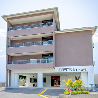 介護施設の建物外観。4階建てで複数のバルコニーと1階の受付エントランスが見える